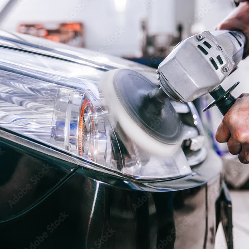 Homme polissant le phare brillant d'une voiture noire avec une machine. Le phare est clair et semble neuf après rénovation.